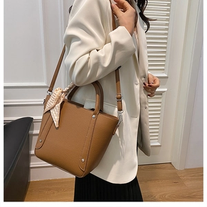 Détail du sac seau en cuir caramel avec rivets argentés et accessoire foulard en soie chic