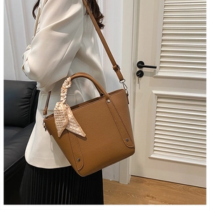 Gros plan du sac seau caramel avec rivets et détail de foulard en soie à motif cœurs