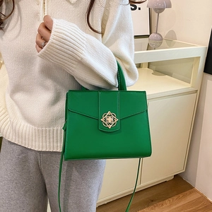 Sac bandoulière chic en cuir vert avec fermoir fleur dorée porté à l'épaule