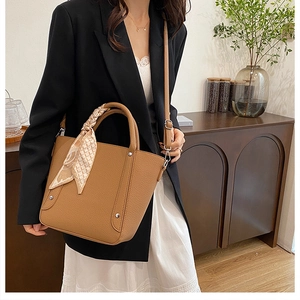 Détail du sac seau marron à motif litchi avec foulard en soie et finitions métalliques