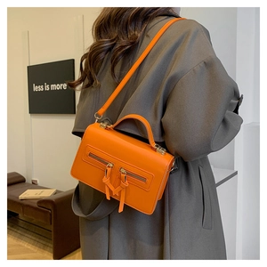 Detail of vintage orange crossbody bag with dual decorative zippers on grey trench coat