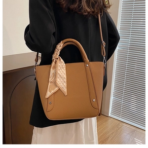 Détail d'un sac seau en cuir marron avec une poignée en foulard et une bandoulière
