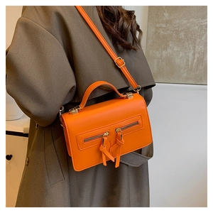 Detail of a vibrant orange crossbody bag with dual zippers and a top handle on a model