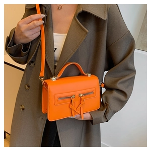 Detail of a bright orange crossbody bag with double front zippers on a trench coat