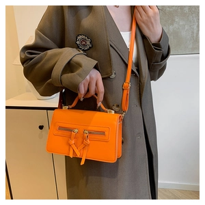 Detail of bright orange leather crossbody bag with dual zipper and thin shoulder strap