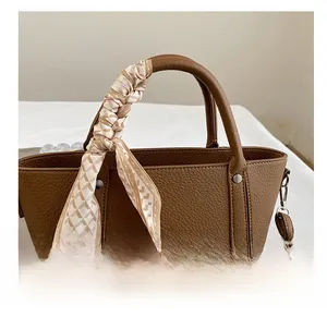 Détail d'un foulard en soie à carreaux géométriques enroulé sur une anse de sac en cuir