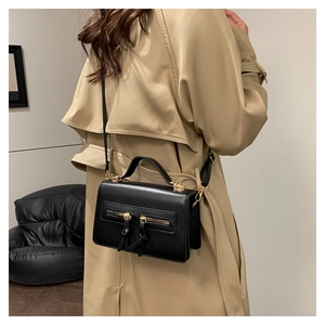 Close-up of a black structured crossbody bag with gold zippers and tassel detail