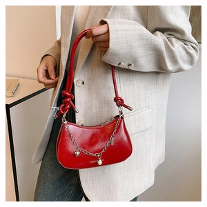 Detail of red glossy leather crescent bag with silver chain, pearl, and heart pendant