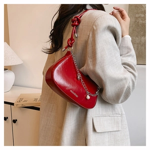 Detail of red patent leather shoulder bag featuring knot strap and pearl chain charm