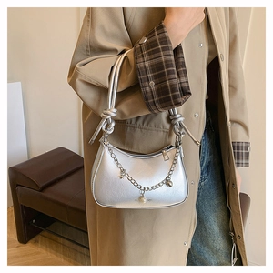 Detail of silver crescent bag with metallic chain charms and knotted strap on trench coat