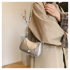 Close-up of silver hobo bag with delicate metal chain, pearl and gold heart pendant
