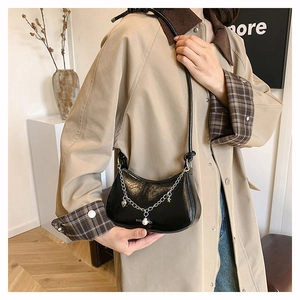 Detail of black glossy crescent bag with silver chain and pearl worn with a khaki trench coat