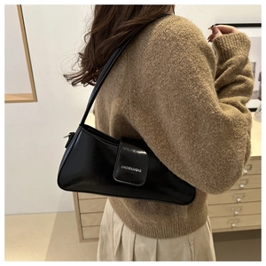 Detailed view of black patent leather baguette bag worn by a model in a cozy home setting