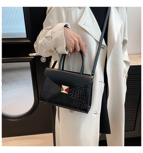Close-up of black crocodile pattern handbag with gold pyramid studs and envelope flap