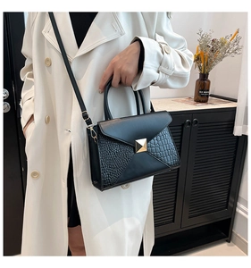 Detail of black crossbody bag with faux crocodile texture and gold square metallic buckle