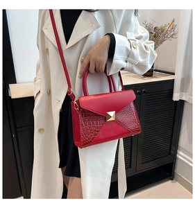 Detail of red crocodile pattern handbag with gold hardware lock on a model outfit