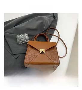 Detail of brown crocodile pattern handbag with large golden square stud and handle