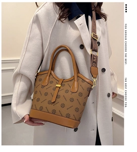 Sac seau vintage marron avec large bandoulière porté par un mannequin en manteau blanc