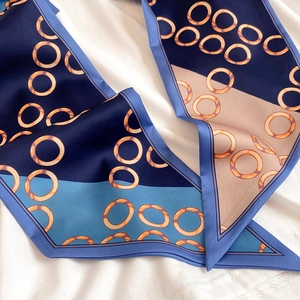Detail eines schmalen Seidenschals mit blau-beigem geometrischem Ringmuster und Glanz