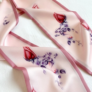 Detailed close-up of pink silk scarf with red rose print and smooth satiny texture