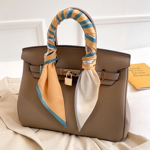 Close-up of a brown leather handbag with a floral silk scarf wrapped around the handle