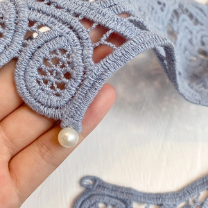 Detail of light blue hollow crochet lace shawl featuring a decorative white pearl accent