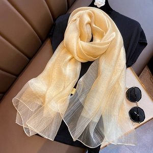 Detail of light gold silk blend scarf with metallic stripes layered on a black shirt