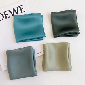Detail view of four shades of green silk scarves neatly folded on a white background