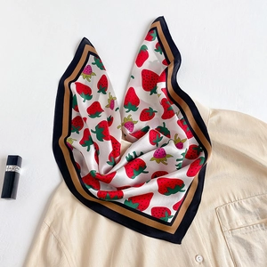 Detail of silk scarf featuring red strawberry prints and contrasting border on a shirt