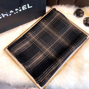 Detail of black and gold checkered silk scarf folded on a white fur mat with sunglasses