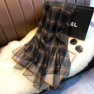 Detail view of lightweight black and bronze metallic checkered scarf on plush cushion