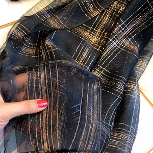 Detailed close-up of translucent black silk blend scarf with metallic gold geometric stripes