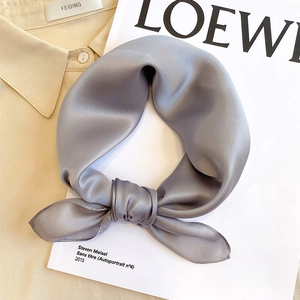 Close-up of a silver-grey silk square scarf tied in a neat bow on a beige shirt collar