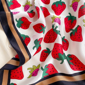 Detail of strawberry print silk scarf featuring elegant black and gold striped border