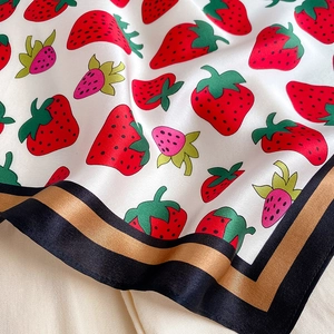 Macro shot of silk scarf showing red strawberry prints and black gold striped border