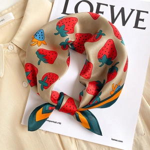 Detail of silk square scarf featuring strawberry print tied on a beige shirt collar