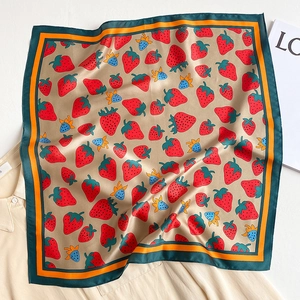 Detailed view of silk square scarf with red strawberry print on light beige fabric