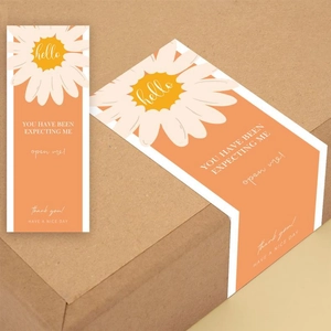 Detail of orange rectangle seal stickers with daisy patterns on a kraft shipping box