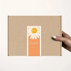 Detail view of an orange daisy sealing sticker on a cardboard box with open me text