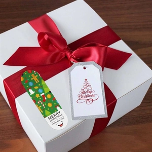 Christmas gift tags and festive stickers on a white gift box with a large red ribbon