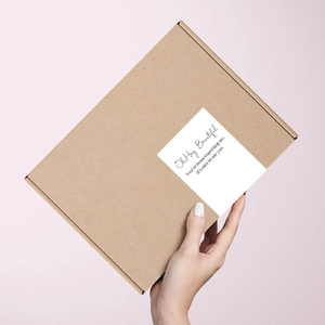 White rectangular thank you label on brown kraft mailing box held against a pink backdrop