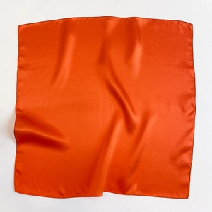 Detail of bright orange silk square scarf showing smooth texture and hemmed edges