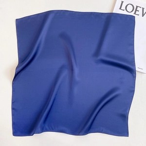 Detailed view of navy blue silk square scarf with glossy finish on a minimalist background