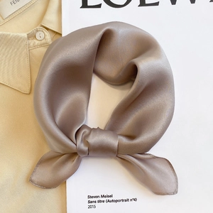 Detail of elegant champagne silk scarf knotted on a beige shirt and white book
