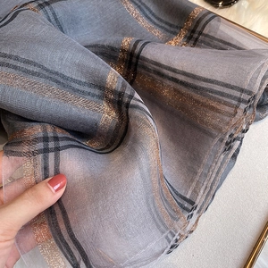Gros plan d'une écharpe à carreaux gris avec fils métalliques et texture soyeuse