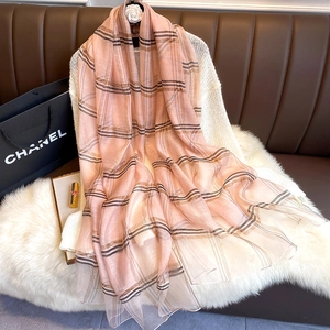 Détail d'une écharpe en soie à carreaux rose et fils dorés sur un pull blanc