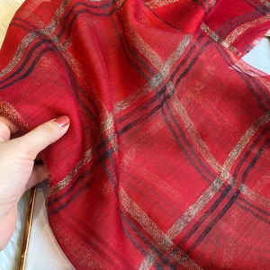 Détail de l'écharpe à carreaux rouges avec fils métalliques brillants et tissu léger