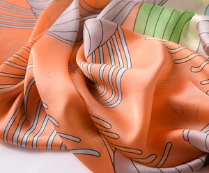Detail view of smooth orange satin scarf with colorful geometric patterns and silky texture