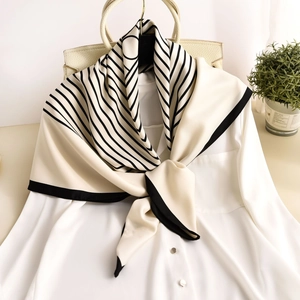 Elegant black and white striped silk-like scarf draped over a white blouse and bag