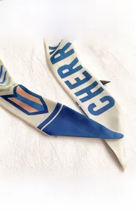 Detail der schmalen Seidenschal-Naht mit blauen Buchstaben auf beigem Grund
